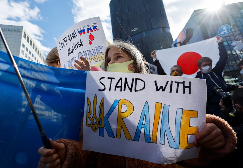 Warga Ukraina yang tinggal di Jepang berdemo memegang plakat dan bendera selama demonstrasi mengecam Rusia atas tindakannya atas Ukraina, di kedutaan Rusia di Tokyo, Jepang, Rabu (23/2/2022). (REUTERS/ISSEI KATO)