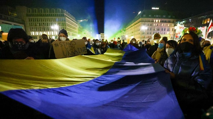 Warga membawa spanduk dan bendera Ukraina di alun-alun di samping Gerbang Brandenburg selama protes anti-perang, setelah Rusia melancarkan operasi militer besar-besaran terhadap Ukraina, di Berlin, Jerman 24 Februari 2022. (REUTERS/FABRIZIO BENSCH)