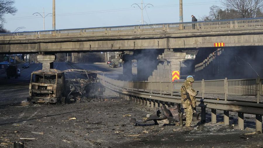 Tentara Ukraina mengambil posisi di luar fasilitas militer saat dua mobil terbakar, di sebuah jalan di Kyiv, Ukraina, Sabtu (26/2/2022). Pasukan Rusia menyerbu ke arah ibu kota Ukraina dan pertempuran jalanan pecah saat pejabat kota mendesak penduduk untuk berlindung. (AP/Emilio Morenatti)
