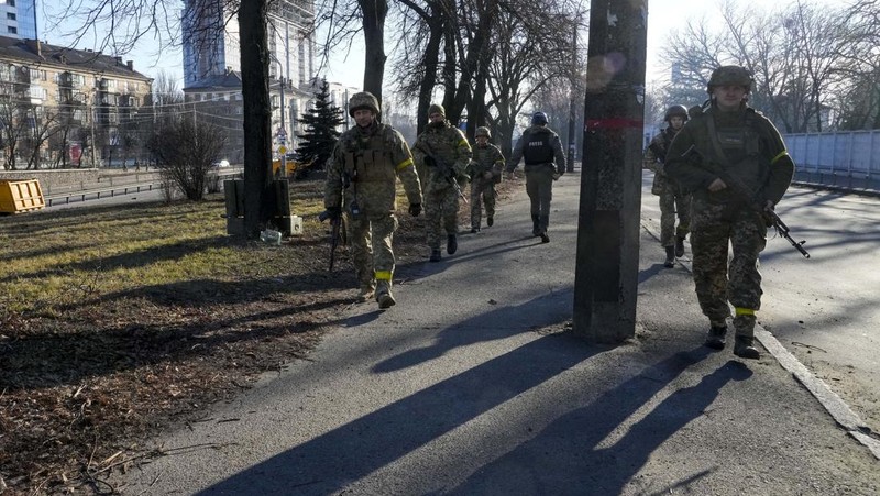 Tentara Ukraina mengambil posisi di luar fasilitas militer saat dua mobil terbakar, di sebuah jalan di Kyiv, Ukraina, Sabtu (26/2/2022). Pasukan Rusia menyerbu ke arah ibu kota Ukraina dan pertempuran jalanan pecah saat pejabat kota mendesak penduduk untuk berlindung. (AP/Emilio Morenatti)