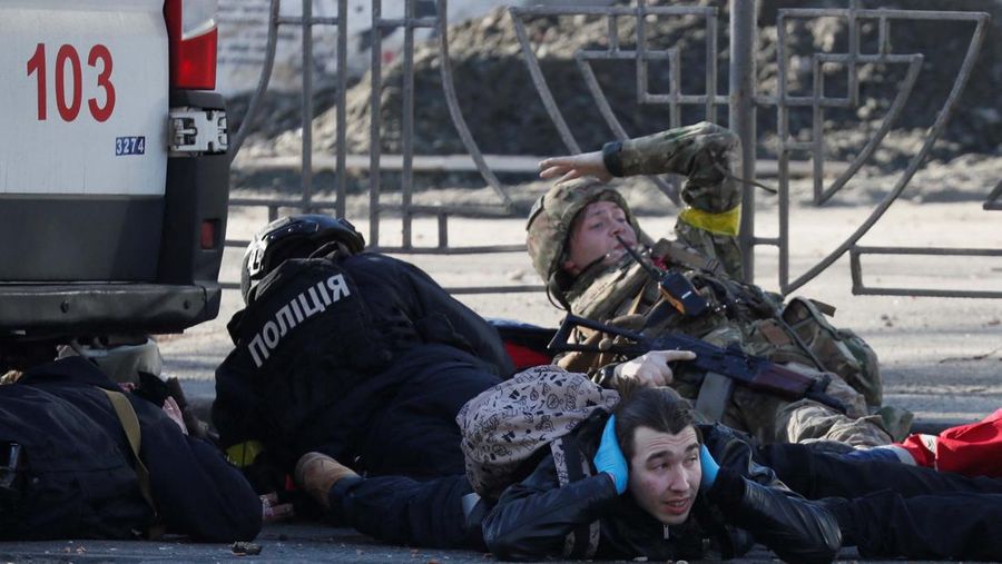 Tentara Ukraina mengambil posisi di luar fasilitas militer saat dua mobil terbakar, di sebuah jalan di Kyiv, Ukraina, Sabtu (26/2/2022). Pasukan Rusia menyerbu ke arah ibu kota Ukraina dan pertempuran jalanan pecah saat pejabat kota mendesak penduduk untuk berlindung. (AP/Emilio Morenatti)