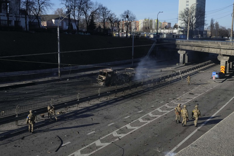 Tentara Ukraina mengambil posisi di luar fasilitas militer saat dua mobil terbakar, di sebuah jalan di Kyiv, Ukraina, Sabtu (26/2/2022). Pasukan Rusia menyerbu ke arah ibu kota Ukraina dan pertempuran jalanan pecah saat pejabat kota mendesak penduduk untuk berlindung. (AP/Emilio Morenatti)