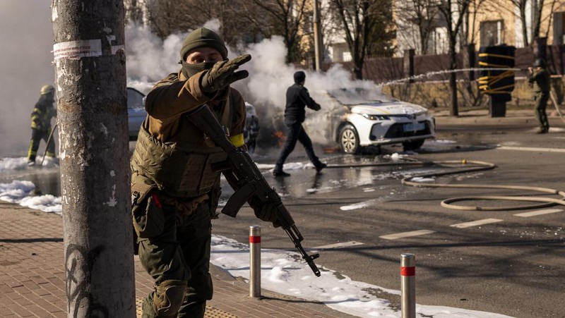 Tentara Ukraina mengambil posisi di luar fasilitas militer saat dua mobil terbakar, di sebuah jalan di Kyiv, Ukraina, Sabtu (26/2/2022). Pasukan Rusia menyerbu ke arah ibu kota Ukraina dan pertempuran jalanan pecah saat pejabat kota mendesak penduduk untuk berlindung. (AP/Emilio Morenatti)