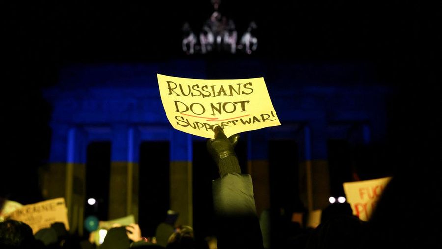 Seseorang memegang poster di depan Gerbang Brandenburg yang menyala dengan warna bendera Ukraina selama protes anti-perang, setelah Rusia melancarkan operasi militer besar-besaran terhadap Ukraina, di Berlin, Jerman, Kamis (24/2/2022). (REUTERS/Christian Mang)