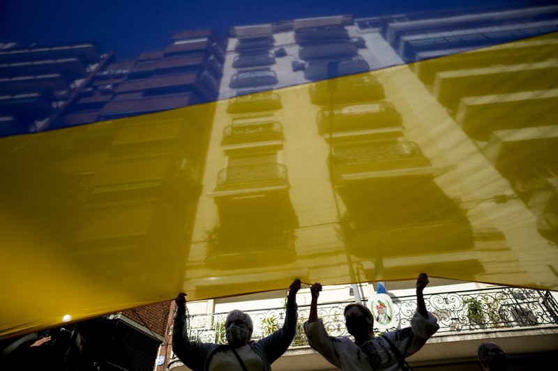 Para wanita membantu mengangkat bendera nasional Ukraina saat mereka memprotes invasi Rusia ke Ukraina, di Buenos Aires, Argentina. Jumat (25/2/2022).  (AP Photo'/Natacha Pisarenko)