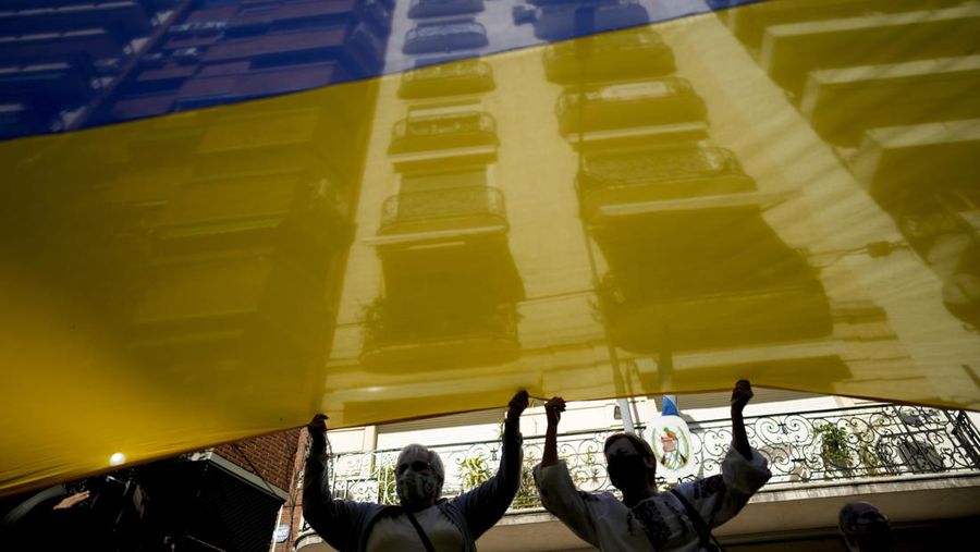 Para wanita membantu mengangkat bendera nasional Ukraina saat mereka memprotes invasi Rusia ke Ukraina, di Buenos Aires, Argentina. Jumat (25/2/2022).  (AP Photo'/Natacha Pisarenko)