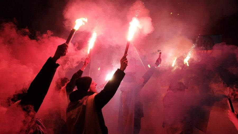 Para wanita membantu mengangkat bendera nasional Ukraina saat mereka memprotes invasi Rusia ke Ukraina, di Buenos Aires, Argentina. Jumat (25/2/2022).  (AP Photo'/Natacha Pisarenko)
