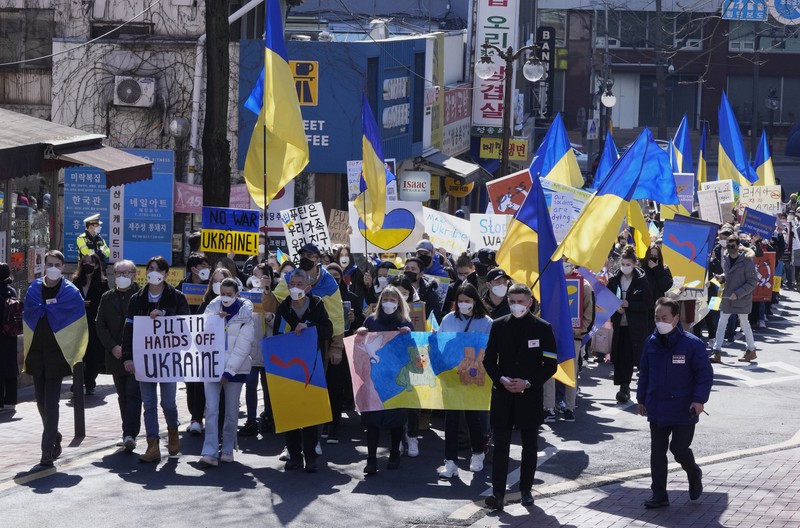 Para wanita membantu mengangkat bendera nasional Ukraina saat mereka memprotes invasi Rusia ke Ukraina, di Buenos Aires, Argentina. Jumat (25/2/2022).  (AP Photo'/Natacha Pisarenko)