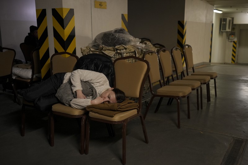 Seorang wanita tidur di kursi di tempat parkir bawah tanah hotel yang berubah menjadi tempat perlindungan bom selama serangan udara Rusia di Kyiv, Ukraina, Minggu (27/2/2022). Pria, wanita, dan anak-anak yang ketakutan mencari keselamatan di dalam dan di bawah tanah, dan pemerintah mempertahankan jam malam 39 jam untuk menjauhkan orang-orang dari jalanan karena lebih dari 150.000 orang Ukraina melarikan diri ke negara-negara tetangga dan PBB memperingatkan jumlah itu bisa bertambah menjadi 4 juta jika pertempuran meningkat. (AP Photo/Vadim Ghirda)