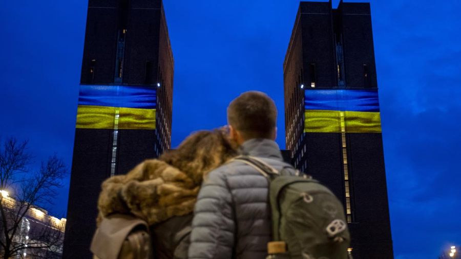 Seorang pria berlari di sepanjang trotoar di seberang Gedung Opera yang diterangi dengan warna bendera nasional Ukraina sebagai dukungan solidaritas atas invasi Rusia di Sydney, Australia, Senin (28/2/2022). (AP Photo /Mark Baker)
