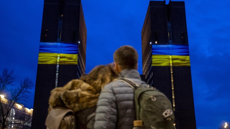 Seorang pria berlari di sepanjang trotoar di seberang Gedung Opera yang diterangi dengan warna bendera nasional Ukraina sebagai dukungan solidaritas atas invasi Rusia di Sydney, Australia, Senin (28/2/2022). (AP Photo /Mark Baker)