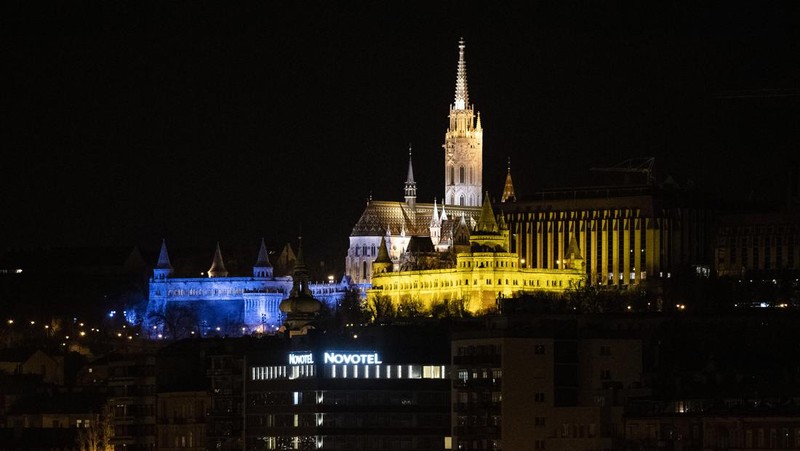 Seorang pria berlari di sepanjang trotoar di seberang Gedung Opera yang diterangi dengan warna bendera nasional Ukraina sebagai dukungan solidaritas atas invasi Rusia di Sydney, Australia, Senin (28/2/2022). (AP Photo /Mark Baker)
