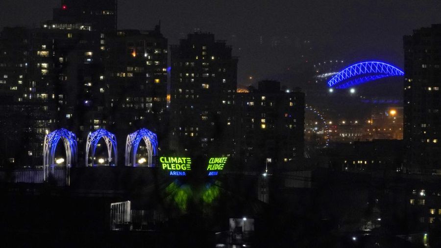 Seorang pria berlari di sepanjang trotoar di seberang Gedung Opera yang diterangi dengan warna bendera nasional Ukraina sebagai dukungan solidaritas atas invasi Rusia di Sydney, Australia, Senin (28/2/2022). (AP Photo /Mark Baker)