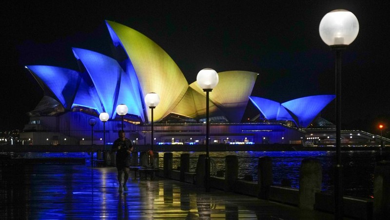 Seorang pria berlari di sepanjang trotoar di seberang Gedung Opera yang diterangi dengan warna bendera nasional Ukraina sebagai dukungan solidaritas atas invasi Rusia di Sydney, Australia, Senin (28/2/2022). (AP Photo /Mark Baker)