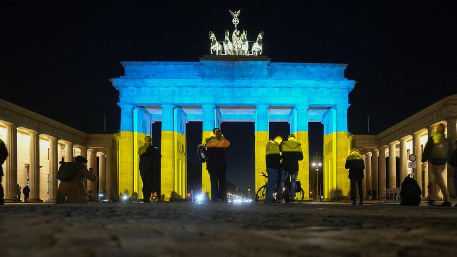 Seorang pria berlari di sepanjang trotoar di seberang Gedung Opera yang diterangi dengan warna bendera nasional Ukraina sebagai dukungan solidaritas atas invasi Rusia di Sydney, Australia, Senin (28/2/2022). (AP Photo /Mark Baker)