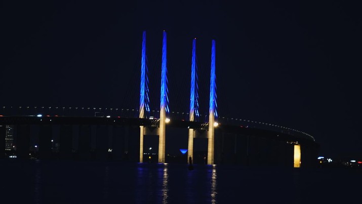 Tiang setinggi 200 meter di Jembatan Oeresund, antara Denmark dan Swedia, menyala dengan warna bendera Ukraina, terlihat dari Kopenhagen, Sabtu (26/2/2022). (Martin Sylvest/Ritzau Scanpix via AP)