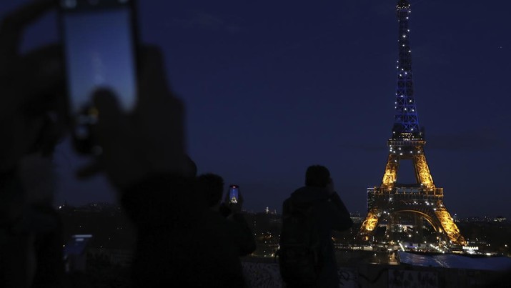 Orang-orang memotret Menara Eiffel yang diterangi dengan warna bendera Ukraina di Paris, Jumat (25/2/2022). (AP Photo/Adrienne Surprenant)