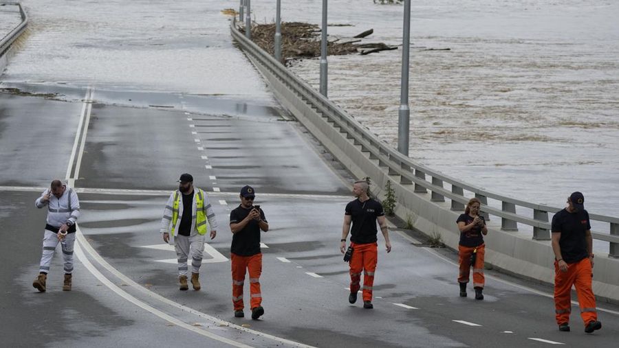 State emergency staff stand near the entrance to the flooded Windsor bridge on the outskirts of Sydney, Australia, Thursday, March 3, 2022. Around 500,000 people in Sydney and its surrounds have been told to evacuate or prepare to flee floodwaters as torrential rain lashes an extraordinarily long stretch of the Australian east coast. (AP Photo/Rick Rycroft)