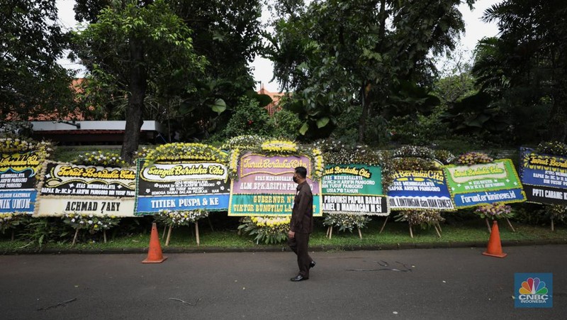 Warga melewati karangan bunga ucapan duka cita di halaman rumah duka almarhum Arifin Panigoro di Griya Jenggala, Jakarta, Senin (7/3/2022). Anggota Dewan Pertimbangan Presiden (Wantimpres) Arifin Panigoro meninggal dunia di Amerika Serikat pada Minggu (6/3/2022). Menurut penjaga keamanan setempat 