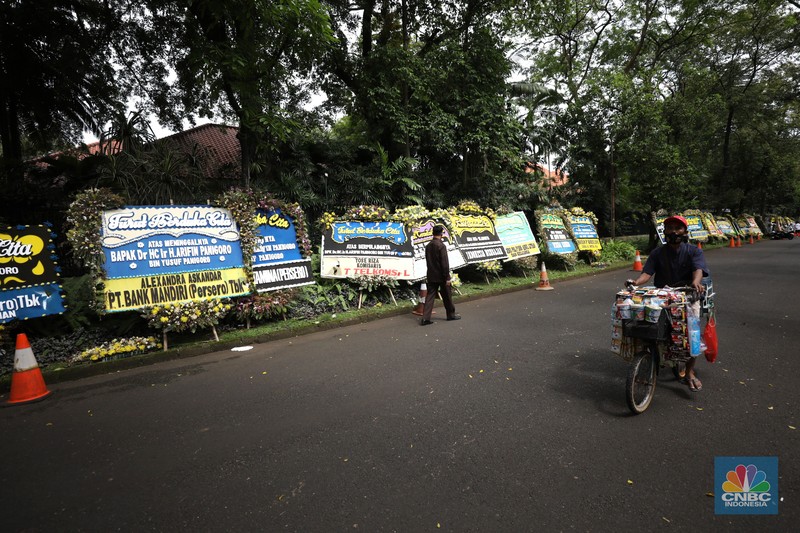 Warga melewati karangan bunga ucapan duka cita di halaman rumah duka almarhum Arifin Panigoro di Griya Jenggala, Jakarta, Senin (7/3/2022). Anggota Dewan Pertimbangan Presiden (Wantimpres) Arifin Panigoro meninggal dunia di Amerika Serikat pada Minggu (6/3/2022). Menurut penjaga keamanan setempat 