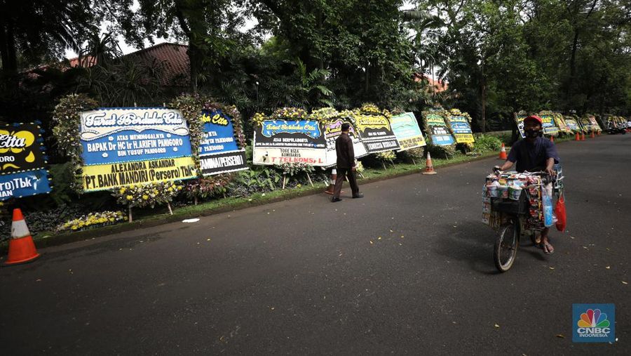 Warga melewati karangan bunga ucapan duka cita di halaman rumah duka almarhum Arifin Panigoro di Griya Jenggala, Jakarta, Senin (7/3/2022). Anggota Dewan Pertimbangan Presiden (Wantimpres) Arifin Panigoro meninggal dunia di Amerika Serikat pada Minggu (6/3/2022). Menurut penjaga keamanan setempat 