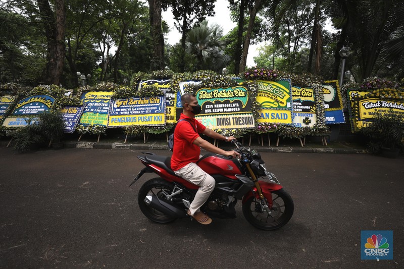 Warga melewati karangan bunga ucapan duka cita di halaman rumah duka almarhum Arifin Panigoro di Griya Jenggala, Jakarta, Senin (7/3/2022). Anggota Dewan Pertimbangan Presiden (Wantimpres) Arifin Panigoro meninggal dunia di Amerika Serikat pada Minggu (6/3/2022). Menurut penjaga keamanan setempat 