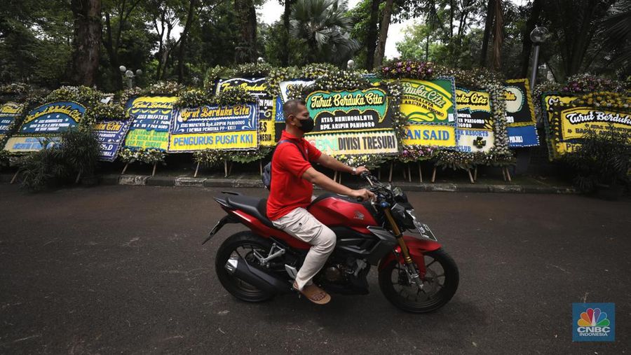 Warga melewati karangan bunga ucapan duka cita di halaman rumah duka almarhum Arifin Panigoro di Griya Jenggala, Jakarta, Senin (7/3/2022). Anggota Dewan Pertimbangan Presiden (Wantimpres) Arifin Panigoro meninggal dunia di Amerika Serikat pada Minggu (6/3/2022). Menurut penjaga keamanan setempat 