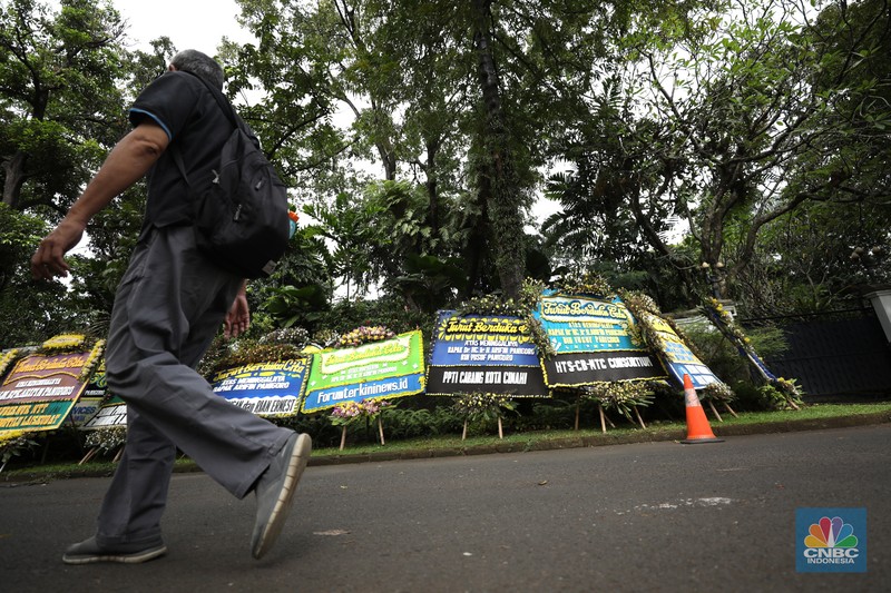 Warga melewati karangan bunga ucapan duka cita di halaman rumah duka almarhum Arifin Panigoro di Griya Jenggala, Jakarta, Senin (7/3/2022). Anggota Dewan Pertimbangan Presiden (Wantimpres) Arifin Panigoro meninggal dunia di Amerika Serikat pada Minggu (6/3/2022). Menurut penjaga keamanan setempat 