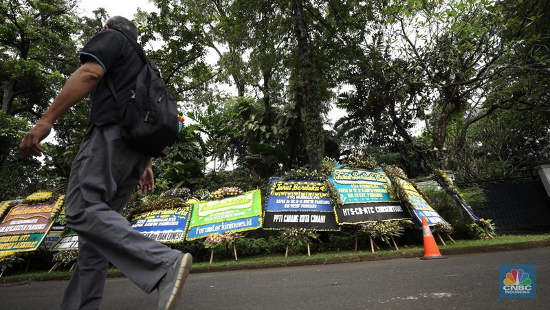 Warga melewati karangan bunga ucapan duka cita di halaman rumah duka almarhum Arifin Panigoro di Griya Jenggala, Jakarta, Senin (7/3/2022). Anggota Dewan Pertimbangan Presiden (Wantimpres) Arifin Panigoro meninggal dunia di Amerika Serikat pada Minggu (6/3/2022). Menurut penjaga keamanan setempat 