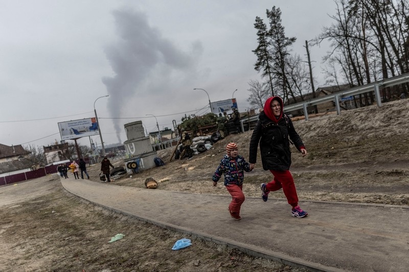 Warga Ukraina melarikan diri untuk evakuasi saat terjadi penyerangan oleh Rusia Warga melintasi jalan setapak di bawah jembatan yang hancur saat melarikan diri dari kota Irpin, Ukraina, MInggu (6/3/2022). Di Irpin, dekat Kyiv, ratusan warga berjalan kaki dan bahkan dengan gerobak dorong melewati sisa-sisa jembatan yang hancur untuk menyeberangi sungai dan meninggalkan kota. (AP Photo/Oleksandr Ratushniak)