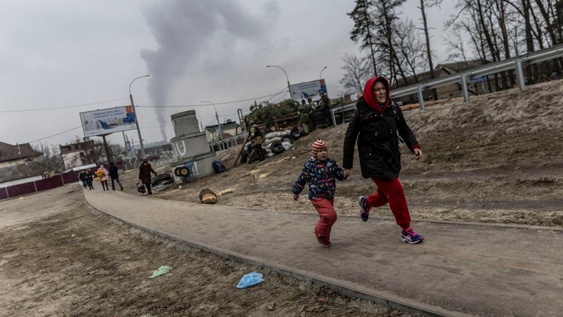 Warga melintasi jalan setapak di bawah jembatan yang hancur saat melarikan diri dari kota Irpin, Ukraina, MInggu (6/3/2022).  Di Irpin, dekat Kyiv, ratusan warga berjalan kaki dan bahkan dengan gerobak dorong melewati sisa-sisa jembatan yang hancur untuk menyeberangi sungai dan meninggalkan kota. (AP Photo/Oleksandr Ratushniak)