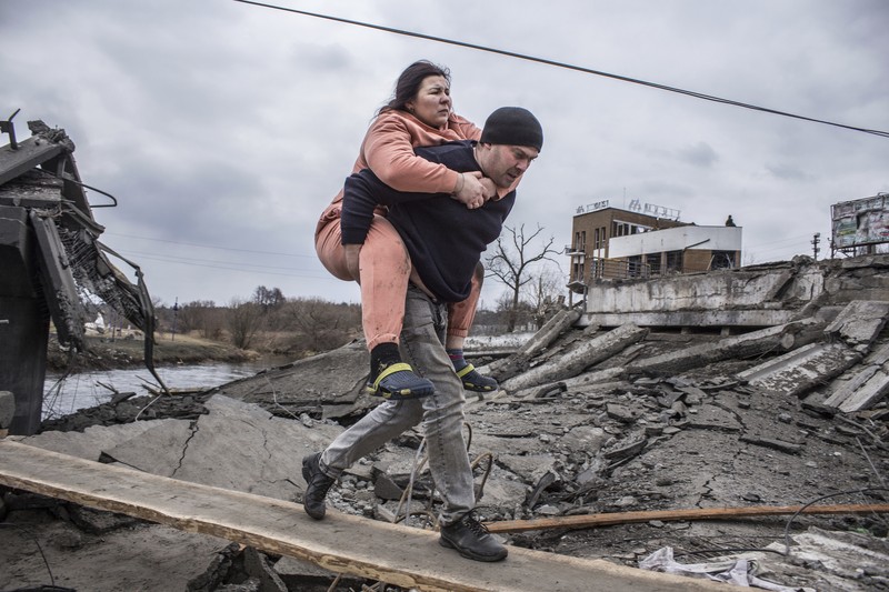 Warga melintasi jalan setapak di bawah jembatan yang hancur saat melarikan diri dari kota Irpin, Ukraina, MInggu (6/3/2022).  Di Irpin, dekat Kyiv, ratusan warga berjalan kaki dan bahkan dengan gerobak dorong melewati sisa-sisa jembatan yang hancur untuk menyeberangi sungai dan meninggalkan kota. (AP Photo/Oleksandr Ratushniak)