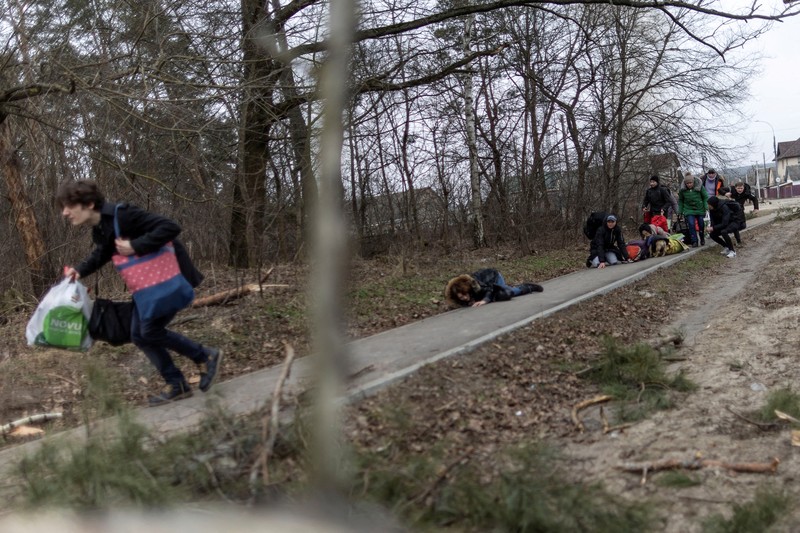 Warga melintasi jalan setapak di bawah jembatan yang hancur saat melarikan diri dari kota Irpin, Ukraina, MInggu (6/3/2022).  Di Irpin, dekat Kyiv, ratusan warga berjalan kaki dan bahkan dengan gerobak dorong melewati sisa-sisa jembatan yang hancur untuk menyeberangi sungai dan meninggalkan kota. (AP Photo/Oleksandr Ratushniak)