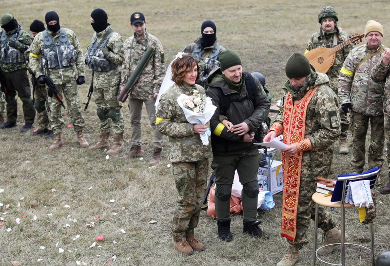 Pernikahan Militer Ukraina Anggota Pasukan Pertahanan Teritorial Ukraina Lesia Ivashchenko dan Valerii Fylymonov mendengarkan seorang pendeta di pernikahan mereka selama konflik Ukraina-Rusia, di sebuah pos pemeriksaan di Kyiv, Ukraina, Minggu (6/3/2022). (REUTERS/Mykola Tymchenko)