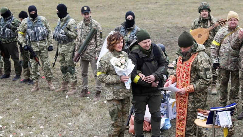 Anggota Pasukan Pertahanan Teritorial Ukraina Lesia Ivashchenko dan Valerii Fylymonov mendengarkan seorang pendeta di pernikahan mereka selama konflik Ukraina-Rusia, di sebuah pos pemeriksaan di Kyiv, Ukraina, Minggu (6/3/2022). (REUTERS/Mykola Tymchenko)