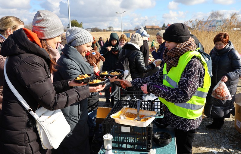 Relawan membagikan makanan kepada orang-orang yang melintasi perbatasan dari Ukraina ke Polandia, setelah melarikan diri dari iserangan Rusia ke Ukraina, di pos pemeriksaan perbatasan di Medyka, Polandia, Selasa (8/3/2022). (REUTERS/Fabrizio Bensch)