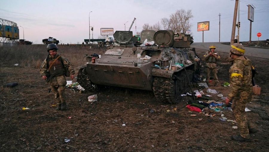Prajurit Ukraina terlihat di sebelah kendaraan lapis baja yang hancur yang mereka katakan milik tentara Rusia di luar Kharkiv, Ukraina, Kamis (24/2/2022). (REUTERS/Maksim Levin)