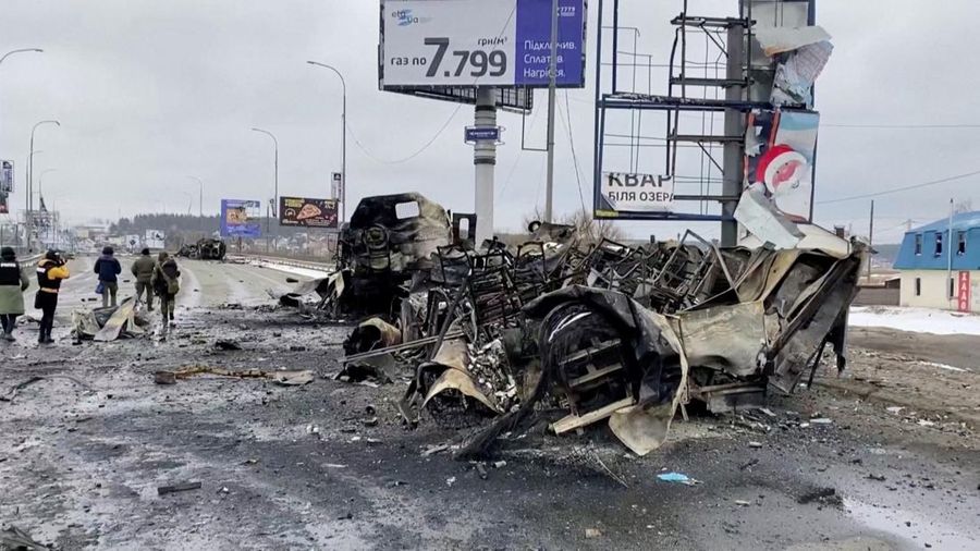 Orang-orang berjalan melewati kendaraan yang hancur di jalan, di tengah serangan Rusia ke Ukraina, di Bucha, Ukraina, Rabu (2/3/2022). (Tangkapan Layar video REUTERS/via Reuters TV)