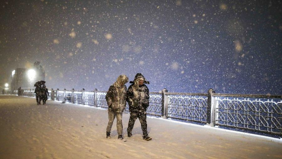 Pedestrians partially covered by snow walk along Galata bridge during a snowfall in Istanbul, Turkey, Saturday, March 12, 2022. (AP Photo/Emrah Gurel)