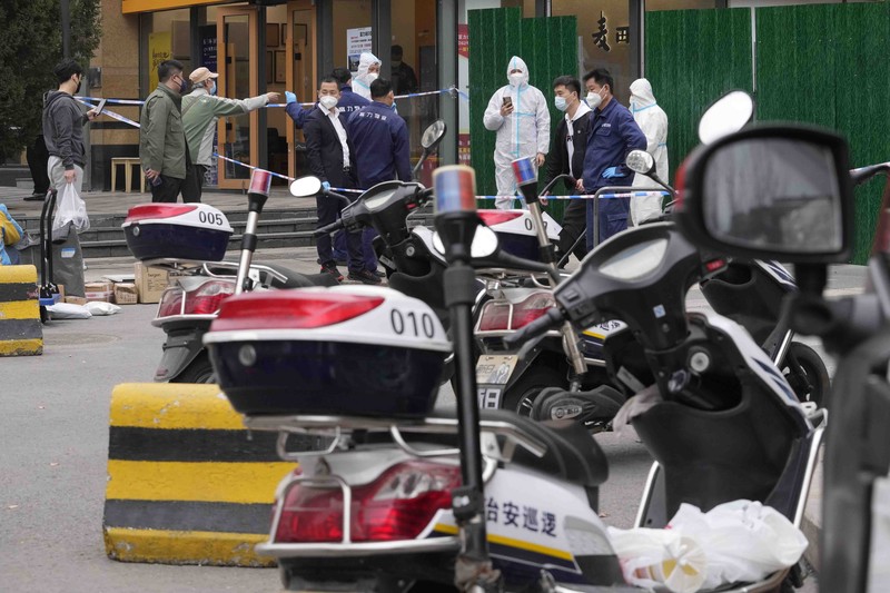 Residents in a locked down community look out from a closed gate as a worker in protective gear monitors access on Sunday, March 13, 2022, in Beijing. The number of new coronavirus cases in an outbreak in China's northeast tripled Sunday and authorities tightened control on access to Shanghai in the east, suspending bus service to the city of 24 million and requiring a virus test for anyone who wants to enter. (AP Photo/Ng Han Guan)