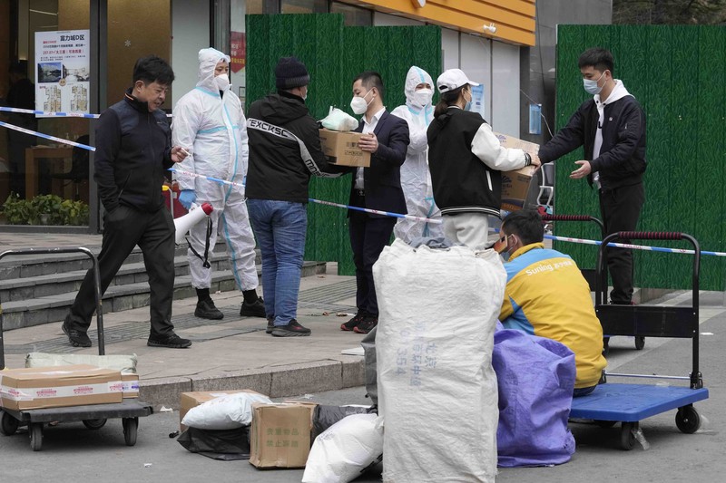 Residents in a locked down community look out from a closed gate as a worker in protective gear monitors access on Sunday, March 13, 2022, in Beijing. The number of new coronavirus cases in an outbreak in China's northeast tripled Sunday and authorities tightened control on access to Shanghai in the east, suspending bus service to the city of 24 million and requiring a virus test for anyone who wants to enter. (AP Photo/Ng Han Guan)