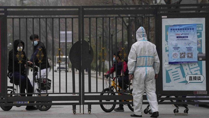 Virus Outbreak China Residents in a locked down community look out from a closed gate as a worker in protective gear monitors access on Sunday, March 13, 2022, in Beijing. The number of new coronavirus cases in an outbreak in China's northeast tripled Sunday and authorities tightened control on access to Shanghai in the east, suspending bus service to the city of 24 million and requiring a virus test for anyone who wants to enter. (AP Photo/Ng Han Guan)