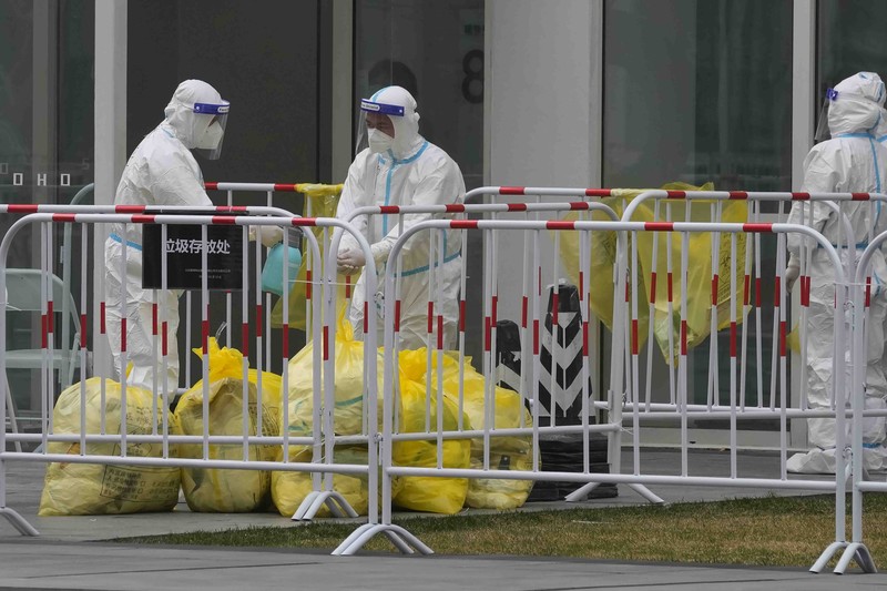 Residents in a locked down community look out from a closed gate as a worker in protective gear monitors access on Sunday, March 13, 2022, in Beijing. The number of new coronavirus cases in an outbreak in China's northeast tripled Sunday and authorities tightened control on access to Shanghai in the east, suspending bus service to the city of 24 million and requiring a virus test for anyone who wants to enter. (AP Photo/Ng Han Guan)