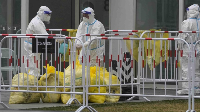 Residents in a locked down community look out from a closed gate as a worker in protective gear monitors access on Sunday, March 13, 2022, in Beijing. The number of new coronavirus cases in an outbreak in China's northeast tripled Sunday and authorities tightened control on access to Shanghai in the east, suspending bus service to the city of 24 million and requiring a virus test for anyone who wants to enter. (AP Photo/Ng Han Guan)