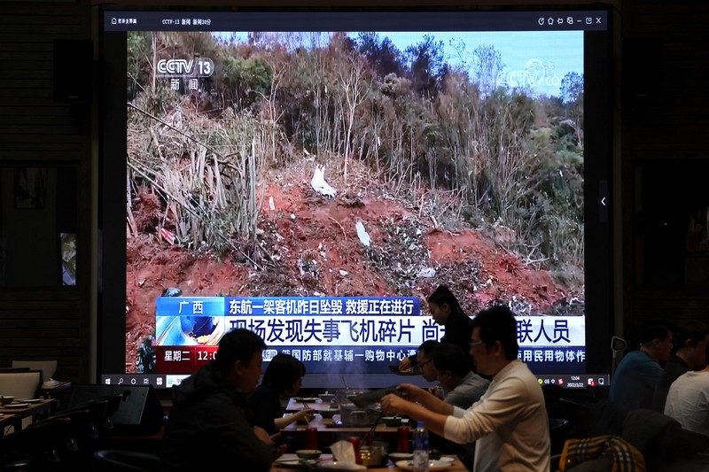 CHINA-CRASH/ A screen shows news footage of plane debris at the site where a China Eastern Airlines Boeing 737-800 plane flying from Kunming to Guangzhou crashed in Wuzhou of Guangxi Zhuang Autonomous Region, while customers dine at a restaurant in Beijing, China March 22, 2022. REUTERS/Tingshu Wang