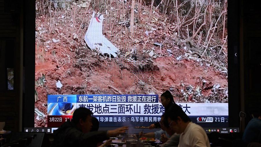 A screen shows news footage of plane debris at the site where a China Eastern Airlines Boeing 737-800 plane flying from Kunming to Guangzhou crashed in Wuzhou of Guangxi Zhuang Autonomous Region, while customers dine at a restaurant in Beijing, China March 22, 2022. REUTERS/Tingshu Wang