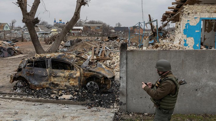 Seorang prajurit Ukraina berjalan melewati mobil yang terbakar, saat serangan Rusia di desa Krasylivka di luar Kyiv, Ukraina 26 Maret 2022. (REUTERS/Marko Djurica)