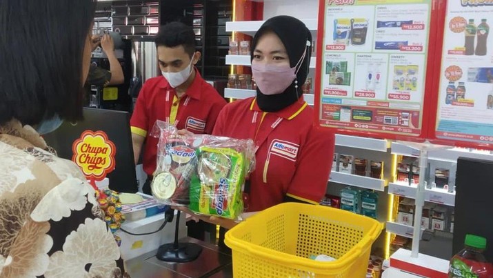 Petugas kasir Alfamart sedang melayani konsumen berbelanja.