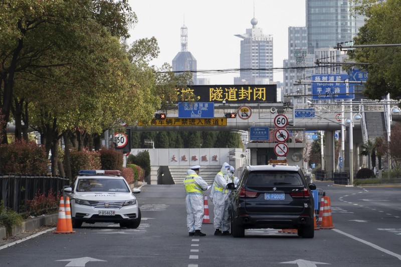 Polisi lalu lintas yang mengenakan pakaian pelindung memeriksa kendaraan sebelum terowongan underpass yang ditutup menyusul penyebaran Covid-19 di Shanghai, China, Senin (28/3/2022).  (Chinatopix Via AP)