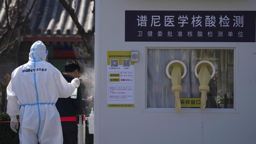 Seorang petugas kesehatan menyemprotkan disinfektan saat seorang warga keluar untuk menjalani tes virus corona di tempat pengujian virus corona swasta, di Beijing, Senin (28/3/2022). (AP Photo/Andy Wong)